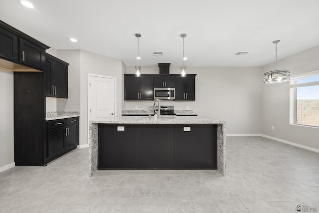 3562 S Sage Ave, Yuma, AZ 85365 - kitchen featuring appliances with stainless steel finishes, dark cabinetry, decorative light fixtures, light stone countertops, and a kitchen island with sink