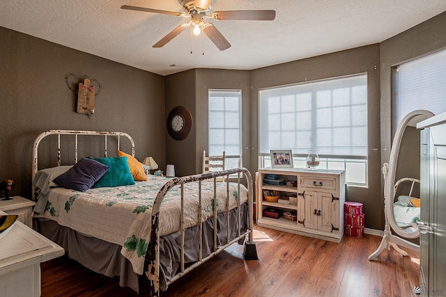 bedroom featuring a ceiling fan, a textured ceiling, a textured wall, and wood finished floors