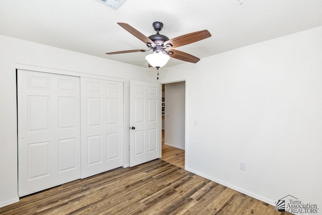 unfurnished bedroom with ceiling fan, visible vents, wood finished floors, baseboards, and a closet