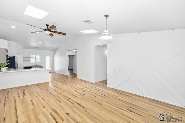 unfurnished living room featuring vaulted ceiling with skylight, a ceiling fan, light wood finished floors, and visible vents