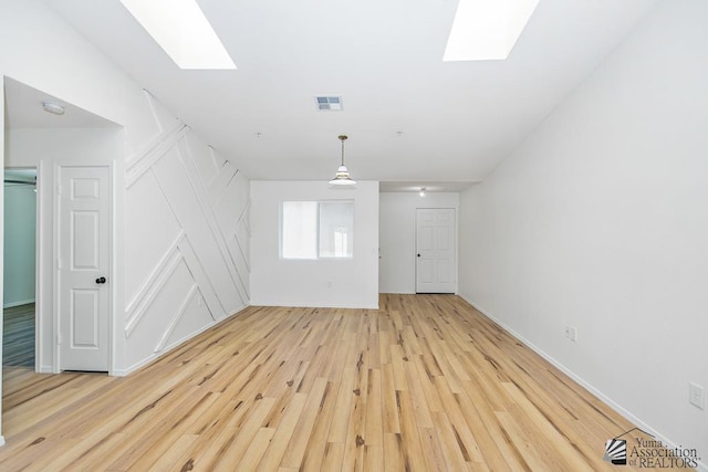 spare room with a skylight, baseboards, light wood-style floors, and visible vents