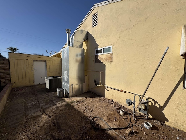 view of side of property featuring an outbuilding, stucco siding, a storage shed, central AC, and fence