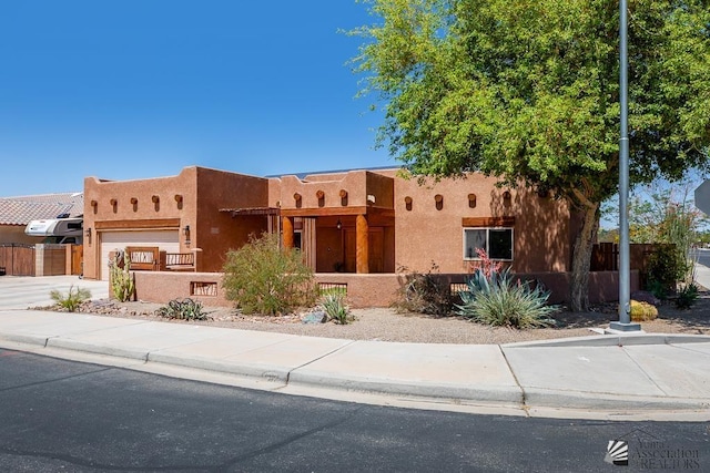 pueblo revival-style home featuring stucco siding, a fenced front yard, and a garage