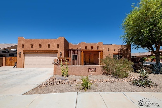 pueblo-style house with a fenced front yard, an attached garage, driveway, and stucco siding