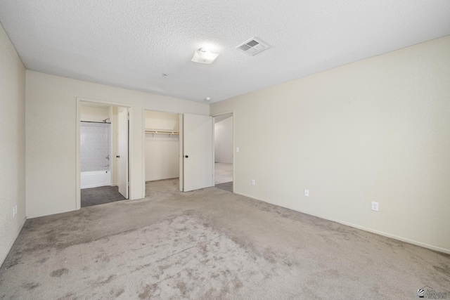 unfurnished bedroom with carpet, connected bathroom, a textured ceiling, a spacious closet, and a closet