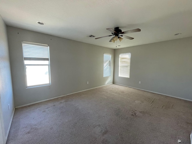 empty room featuring a wealth of natural light, ceiling fan, and light carpet