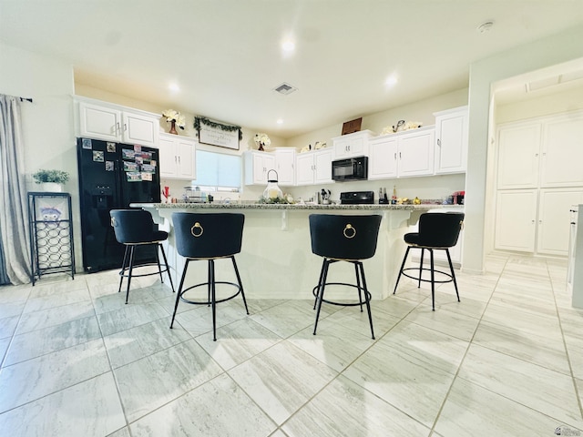 kitchen with black appliances, a kitchen bar, white cabinetry, and visible vents