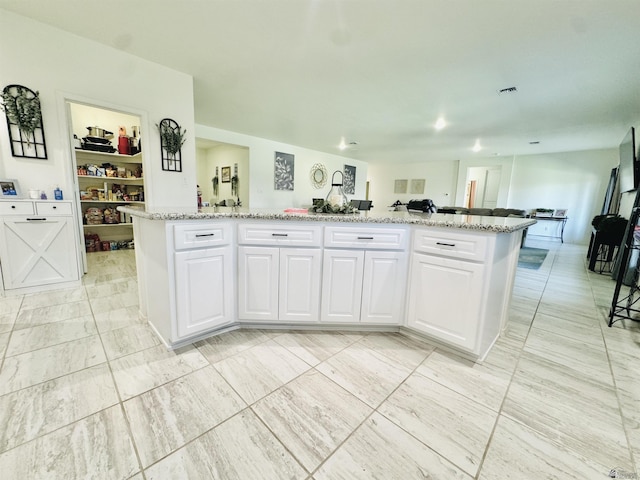 kitchen with a kitchen island, visible vents, light stone counters, open floor plan, and white cabinetry
