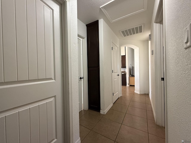 126 N Joe Harper Ct, San Luis, AZ 85349 - hall featuring tile patterned flooring, arched walkways, a textured wall, and baseboards