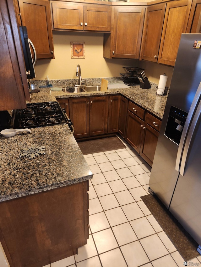 kitchen with light tile patterned flooring, stainless steel fridge, a sink, range with gas stovetop, and dark stone counters