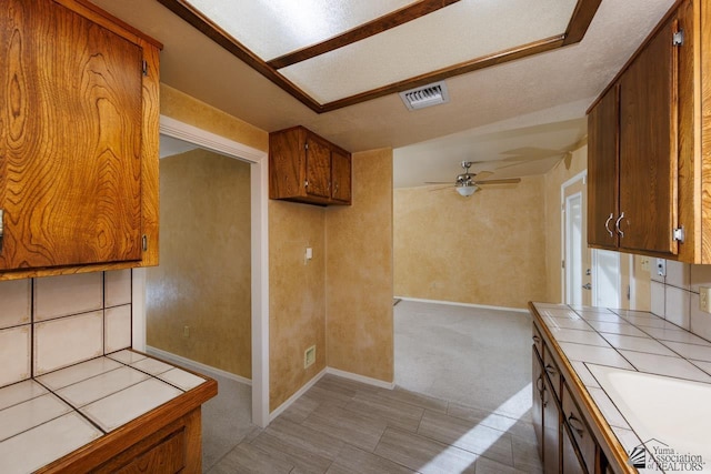 kitchen with visible vents, brown cabinetry, and tile counters