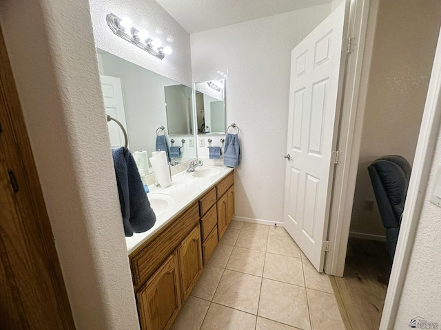 full bathroom with a sink, tile patterned flooring, a textured wall, and double vanity