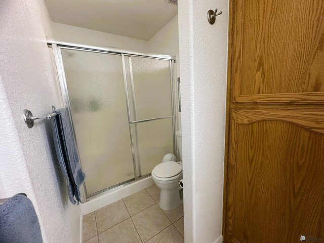 full bath with toilet, tile patterned floors, a textured wall, and a stall shower