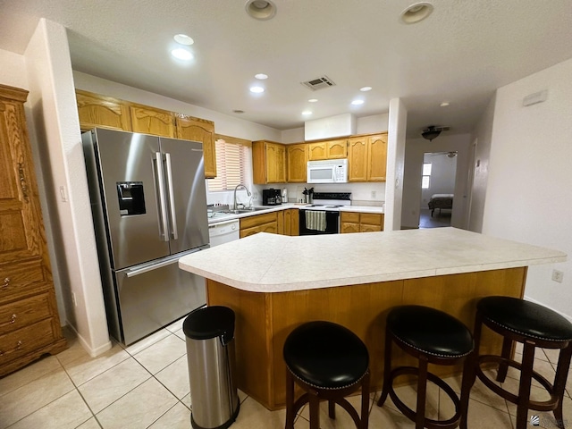 kitchen featuring visible vents, white appliances, a kitchen breakfast bar, light countertops, and a sink
