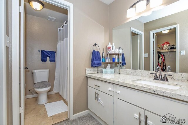 bathroom with vanity, toilet, baseboards, a walk in closet, and tile patterned floors