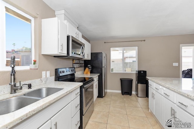 kitchen featuring white cabinetry, light stone counters, a sink, light tile patterned floors, and stainless steel appliances