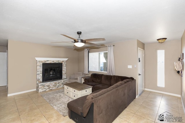 living room featuring light tile patterned floors, baseboards, a ceiling fan, and a stone fireplace