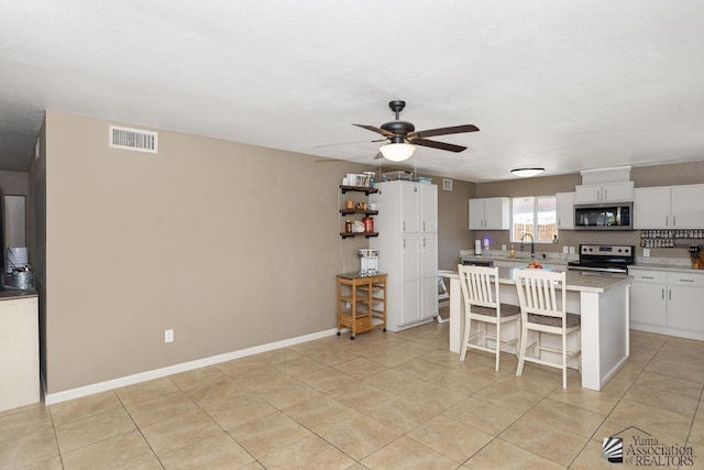 kitchen with ceiling fan, appliances with stainless steel finishes, a breakfast bar, a sink, and visible vents
