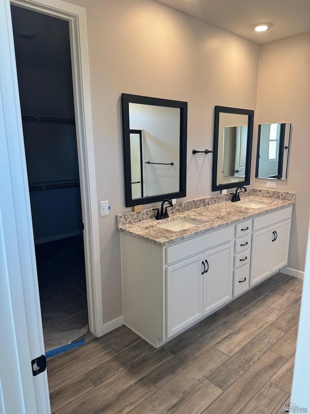 bathroom with a sink, baseboards, double vanity, and wood finished floors