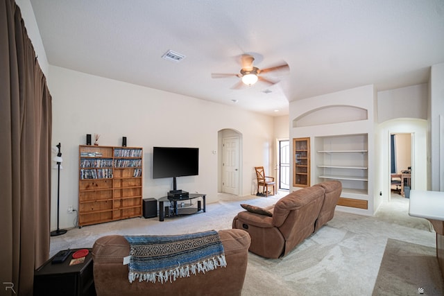 living room with built in features, light colored carpet, and ceiling fan