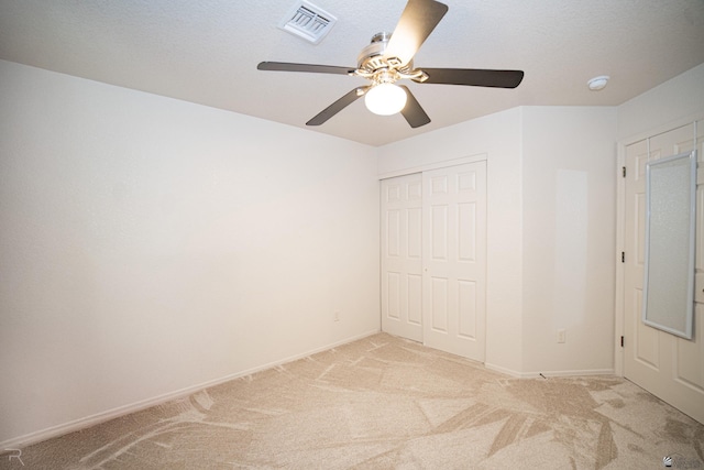 unfurnished bedroom featuring ceiling fan, a closet, light carpet, and a textured ceiling