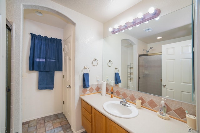 bathroom with vanity, a shower with shower door, decorative backsplash, and a textured ceiling