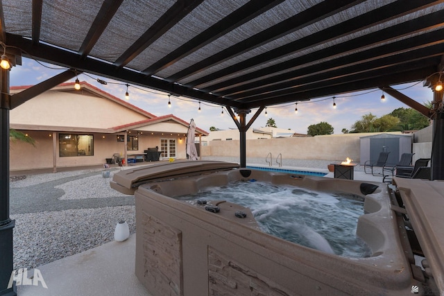 patio terrace at dusk with a hot tub, a fenced backyard, a storage unit, and an outbuilding