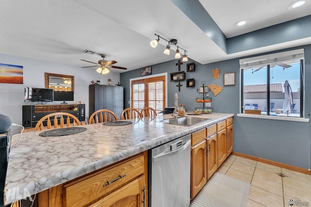 kitchen with light tile patterned floors, baseboards, a peninsula, stainless steel dishwasher, and a sink