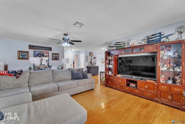 living room with light wood-style floors, visible vents, ceiling fan, and a textured ceiling