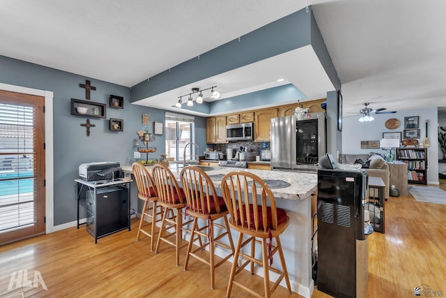 kitchen featuring a tray ceiling, a breakfast bar area, light wood-style flooring, decorative backsplash, and appliances with stainless steel finishes