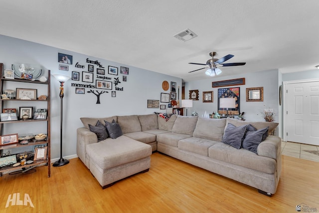 living room featuring light wood-type flooring, visible vents, ceiling fan, and a textured ceiling