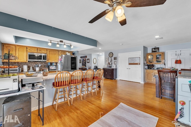 kitchen with tasteful backsplash, appliances with stainless steel finishes, a peninsula, light countertops, and light wood-style floors