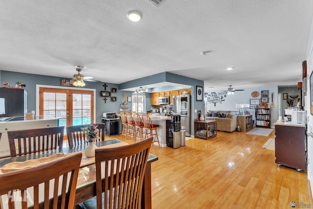 dining room featuring light wood-type flooring, ceiling fan, a textured ceiling, and french doors