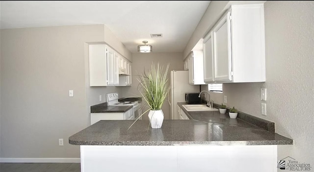 kitchen featuring white range with electric stovetop, a sink, a peninsula, white cabinets, and dark countertops