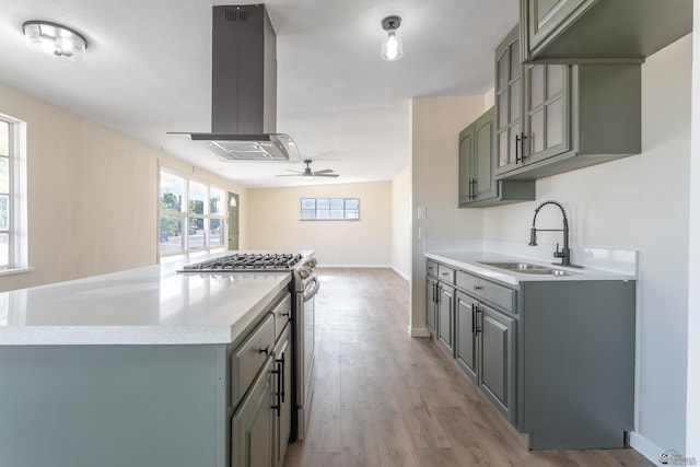 kitchen featuring a sink, stainless steel gas stove, gray cabinets, a ceiling fan, and island range hood