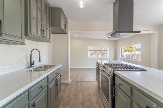 kitchen with island range hood, stainless steel gas stove, a sink, light countertops, and light wood finished floors