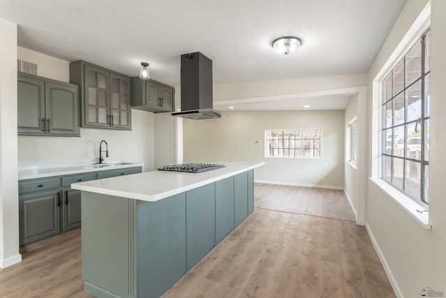 kitchen featuring a sink, light wood-style floors, light countertops, stainless steel gas stovetop, and island exhaust hood