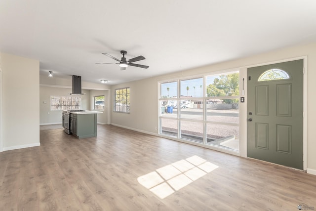 unfurnished living room with ceiling fan, baseboards, and light wood-style flooring