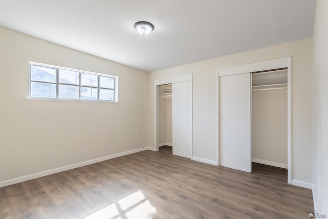 unfurnished bedroom with baseboards, multiple closets, and wood finished floors