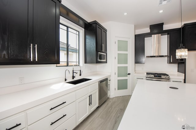 kitchen featuring wall chimney range hood, stainless steel appliances, dark cabinetry, and a sink