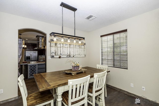 dining room with arched walkways, dark wood finished floors, visible vents, a textured ceiling, and baseboards