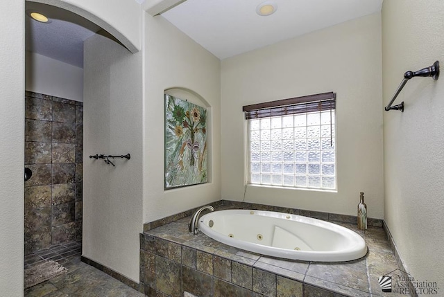 bathroom with stone finish floor, a tub with jets, and a tile shower