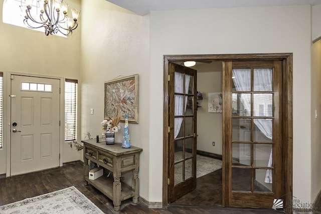 foyer featuring baseboards, french doors, dark wood-type flooring, and an inviting chandelier