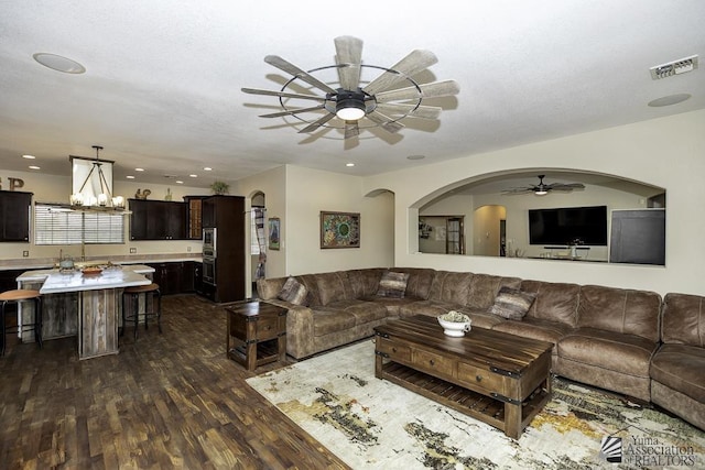 living room with dark wood-style floors, recessed lighting, visible vents, and ceiling fan with notable chandelier