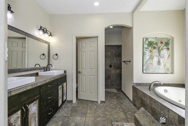 bathroom with a whirlpool tub, stone tile floors, double vanity, and a sink