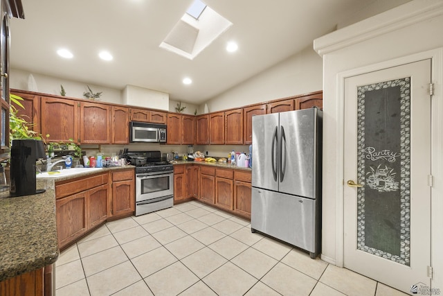 kitchen featuring vaulted ceiling with skylight, brown cabinetry, stainless steel appliances, and light tile patterned flooring