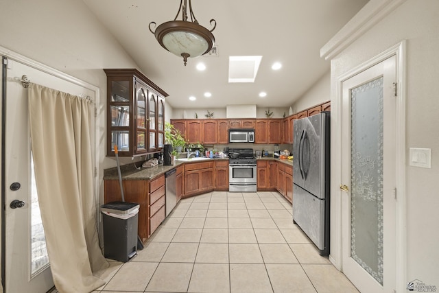 kitchen featuring light tile patterned flooring, appliances with stainless steel finishes, a sink, lofted ceiling, and glass insert cabinets
