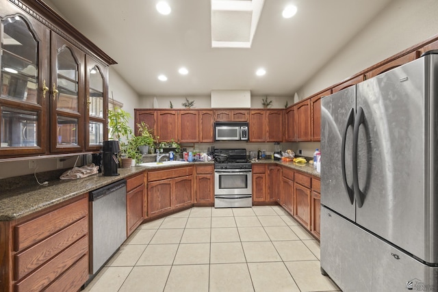kitchen with brown cabinetry, light tile patterned floors, a sink, lofted ceiling, and stainless steel appliances