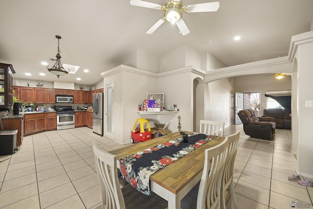 dining area featuring a ceiling fan, arched walkways, vaulted ceiling, and light tile patterned floors