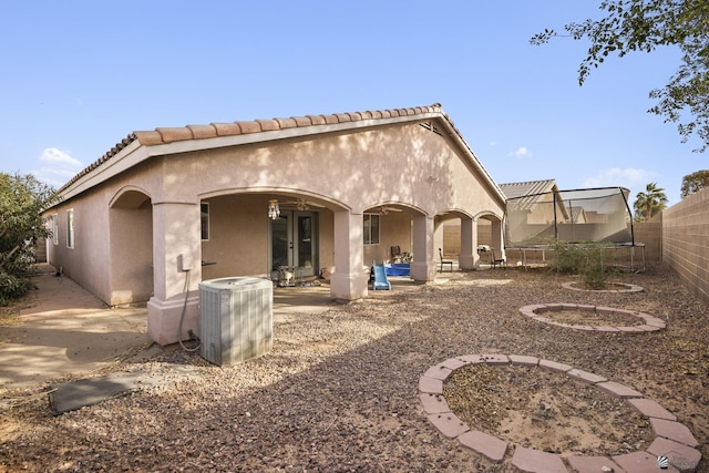 rear view of property featuring a trampoline, stucco siding, a fenced backyard, central air condition unit, and a patio